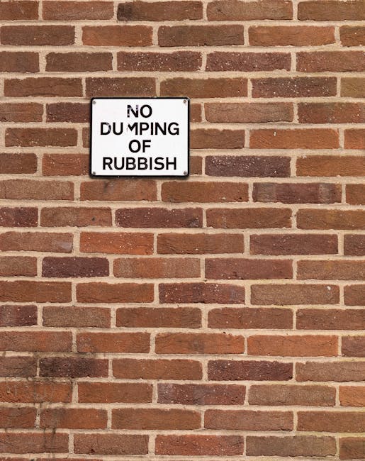 Photograph of a red brick wall with a white rectangular sign mounted on it, displaying the message 'NO DUMPING OF RUBBISH' in black capital letters. The bricks are laid in a traditional running bond p